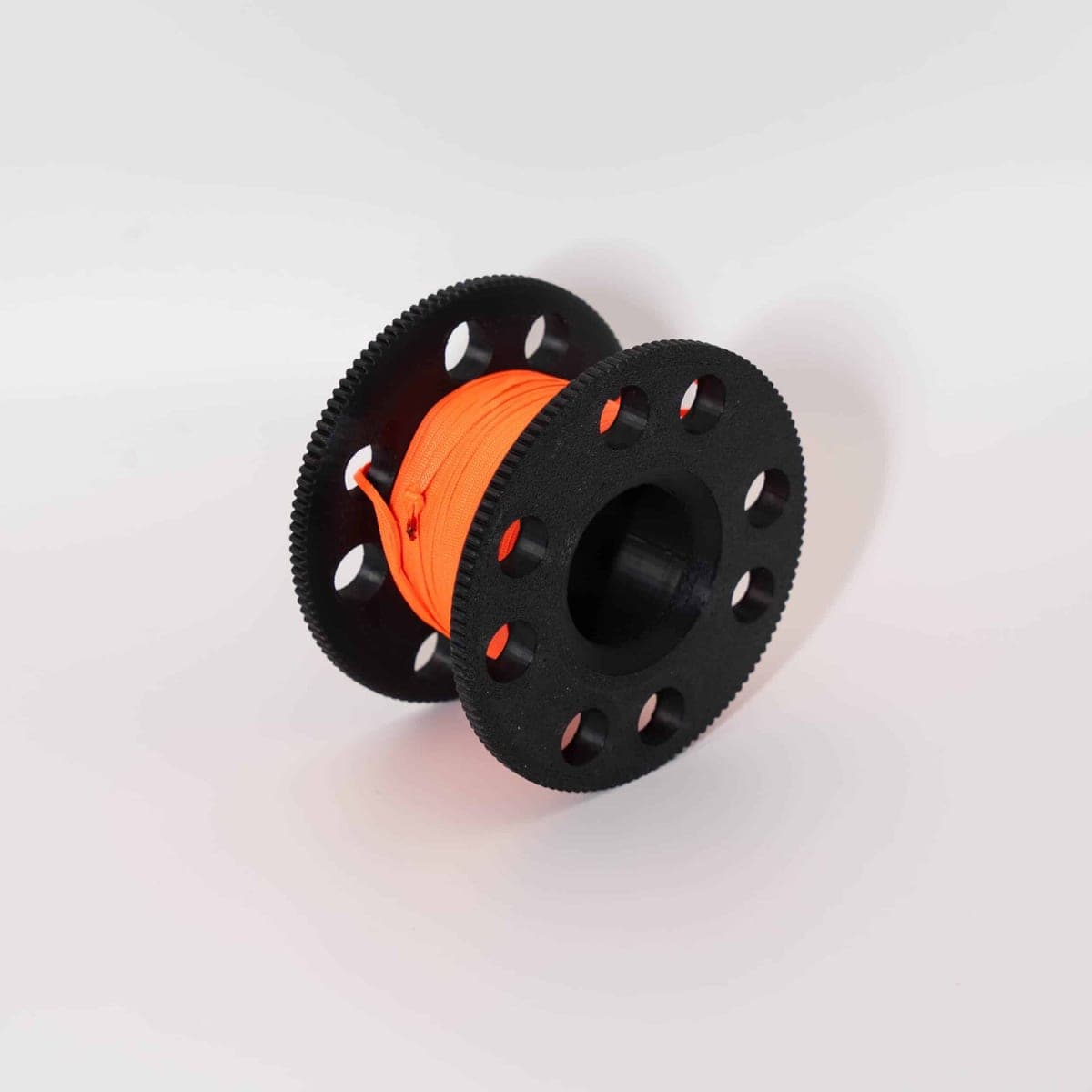 Svart 3D-printad dykreel med räfflade sidor, laddad med orange flatline, mot ljusgrå bakgrund.